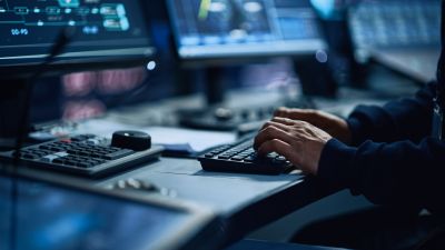 Mann sitzt vor mehreren Bildschirmen und tippt auf Tastatur