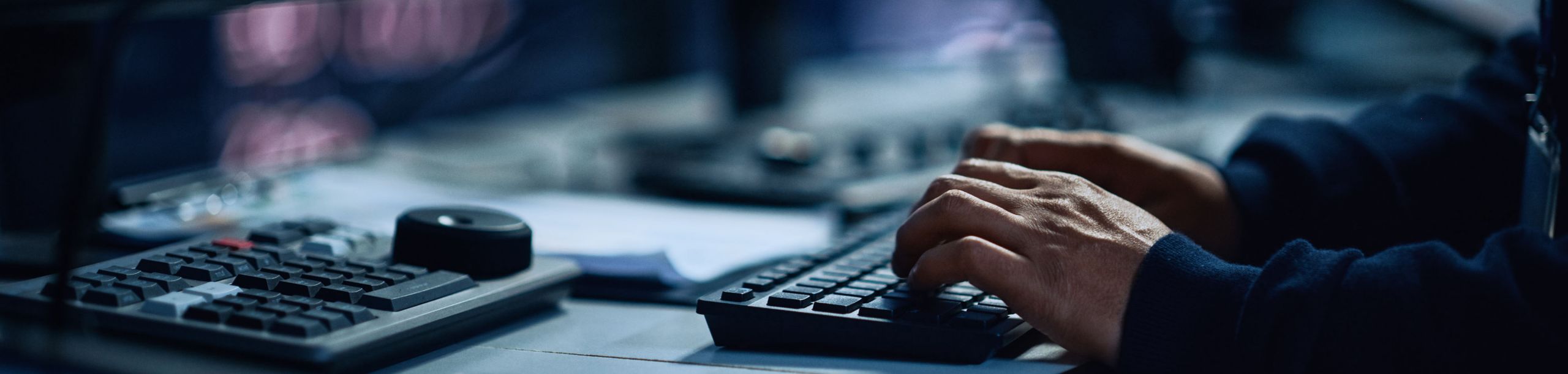 Mann sitzt vor mehreren Bildschirmen und tippt auf Tastatur